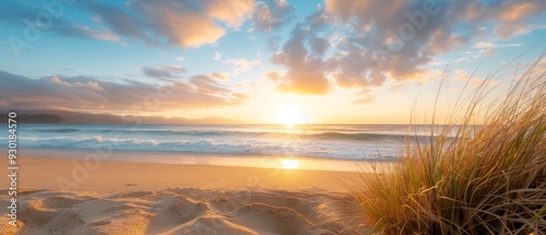 Fototapeta Naklejka Na Ścianę i Meble -   The sun sets over the ocean, featuring a sandy beach in the foreground and grass near the shore