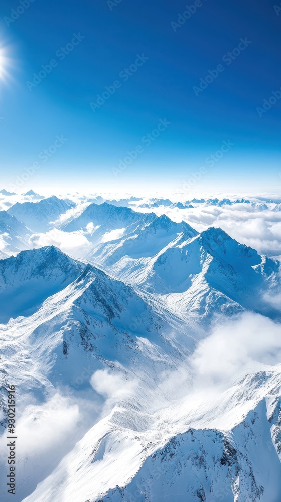 Obraz premium An aerial view of a mountain range with snow-capped peaks, deep valleys, and clouds drifting over the landscape, creating a majestic and awe-inspiring scene