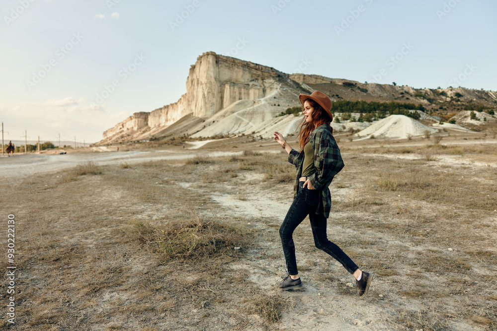 Obraz premium Woman in hat and jeans walking in desert with mountain in background