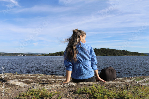 Woman enjoying the view by the lake. Woman sitting in the beach by the fjord in Norway, Oslo.