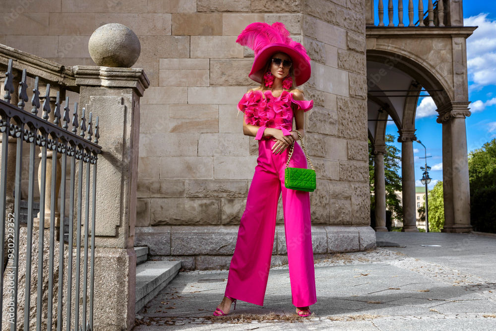 Spring summer fashion. High fashion model. Glamour, stylish elegant woman in pink jumpsuit and big hat. Female model in stylish look in the city. Outdoor shoot. Spring summer fashion. High fashion model. Glamour, stylish elegant woman in pink jumpsuit and big hat. Female model in stylish look in the city. Outdoor shoot.