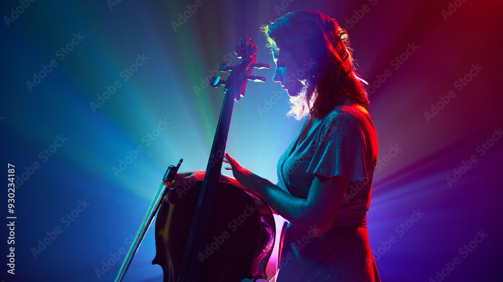 Fototapeta premium Silhouette of artistic woman, musician standing on stage with musical instrument, double bass in vibrant stage lights. Concept of classical and modern music, entertainment, jazz. Ad