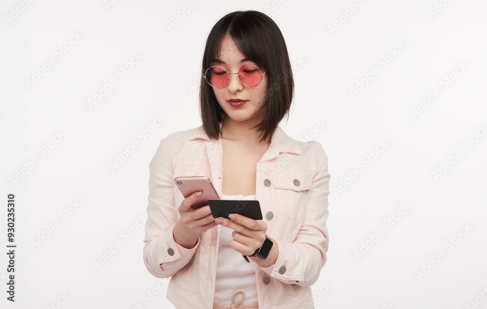 Young woman using a mobile phone and credit card for online shopping. Wearing pink sunglasses and jacket, isolated on white background. Young woman using a mobile phone and credit card for online shopping. Wearing pink sunglasses and jacket, isolated on white background.