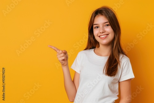 Young woman smiling, pointing to the side, isolated on yellow background with copy space.