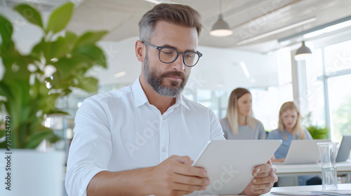 Mature business people using digital tablet while working with colleagues in background at open plan office