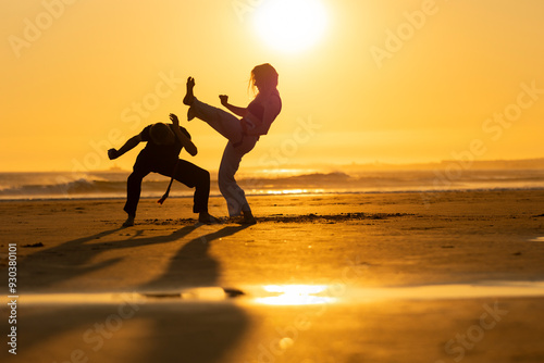Two people practicing capoeira martial arts on the beach at sunset