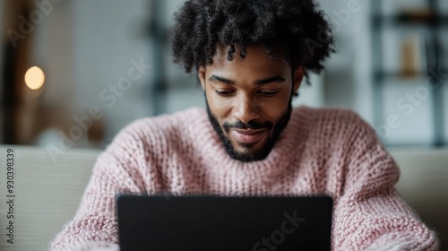 The image captures a person wearing a pink sweater, deeply engaged in work or browsing on a laptop. The background hints at a modern, minimalist workspace setting. photo