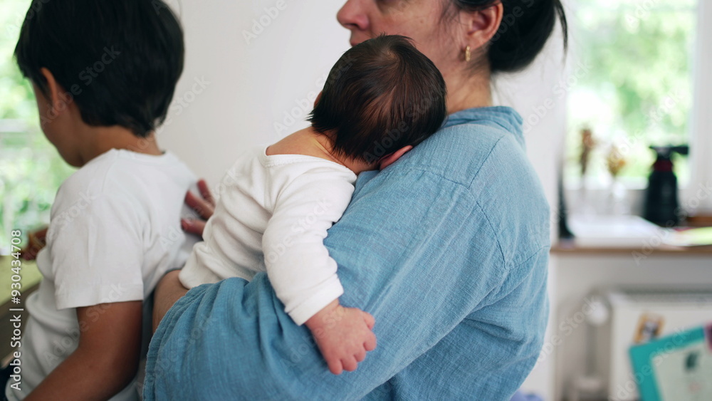 Mother holding newborn baby close while another child stands nearby eating. This image captures the busy and loving dynamics of parenthood in a cozy home environment Mother holding newborn baby close while another child stands nearby eating. This image captures the busy and loving dynamics of parenthood in a cozy home environment