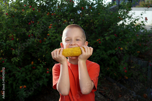 Seven year old happy boy eating sweet corn on the cob in summer garden. Selective focus.