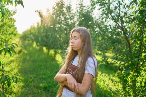 a teenage girl prays with a holy bible in a garden illuminated by light