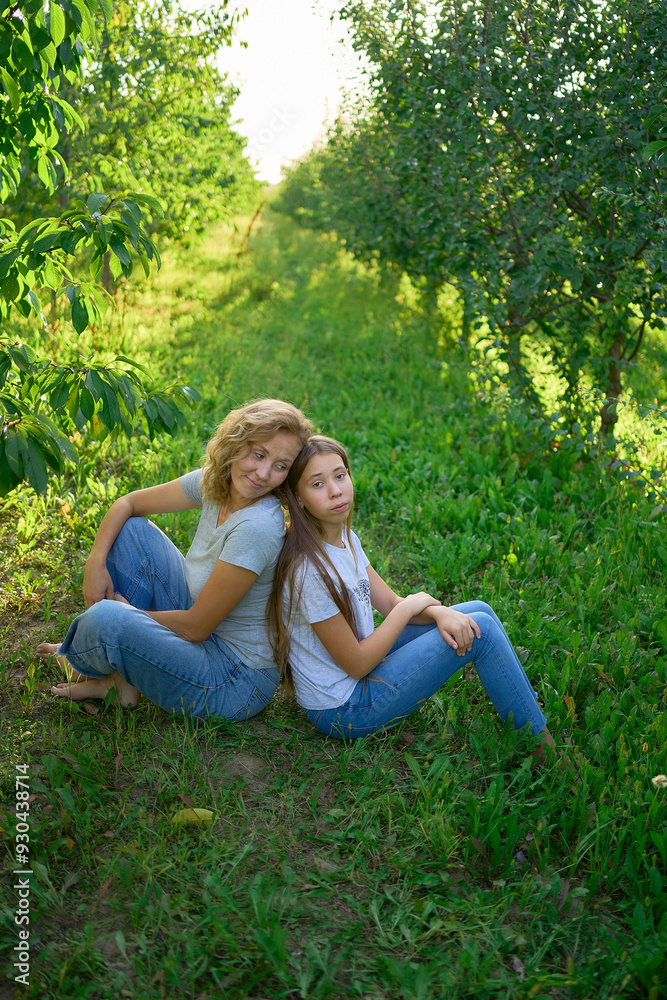 mother and teenage girls with long blond hair spend time together in the sunlit park