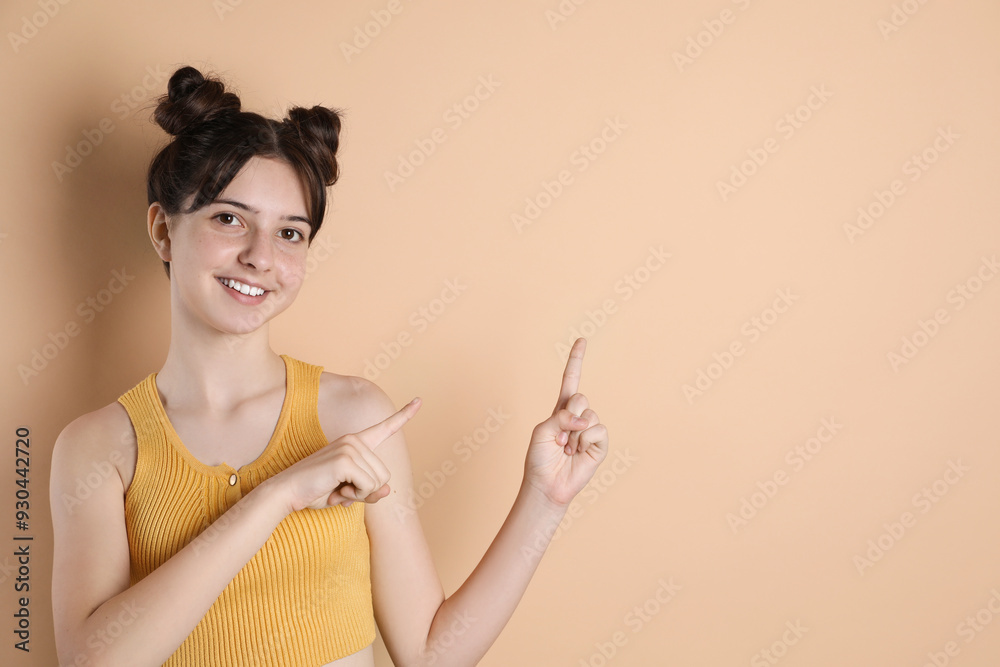Portrait of smiling teenage girl pointing at something on beige background. Space for text Portrait of smiling teenage girl pointing at something on beige background. Space for text