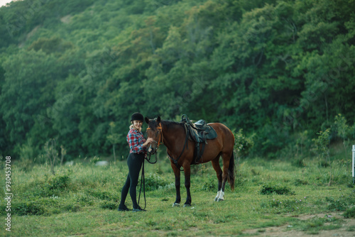 Happy blonde with horse in forest. Woman and a horse walking through the field during the day. Dressed in a plaid shirt and black leggings.