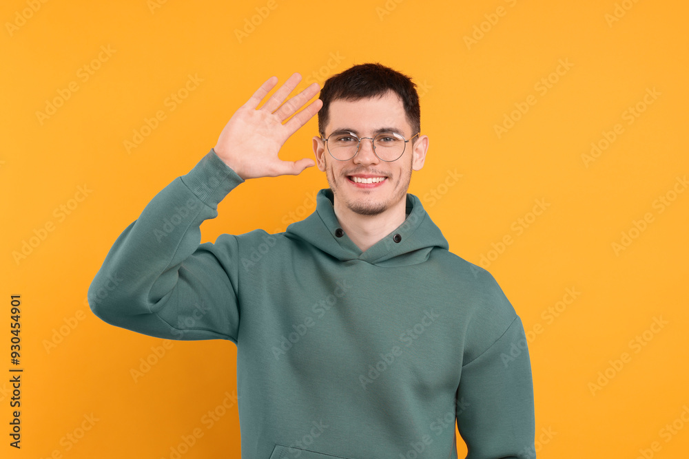 Happy young man waving on orange background Happy young man waving on orange background