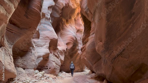 A female hiker walks through the majestic Buckskin Gulch, a deep and narrow slot canyon on the Arizona, Utah border. The towering sandstone walls, sculpted by erosion, create a sense of awe - USA
