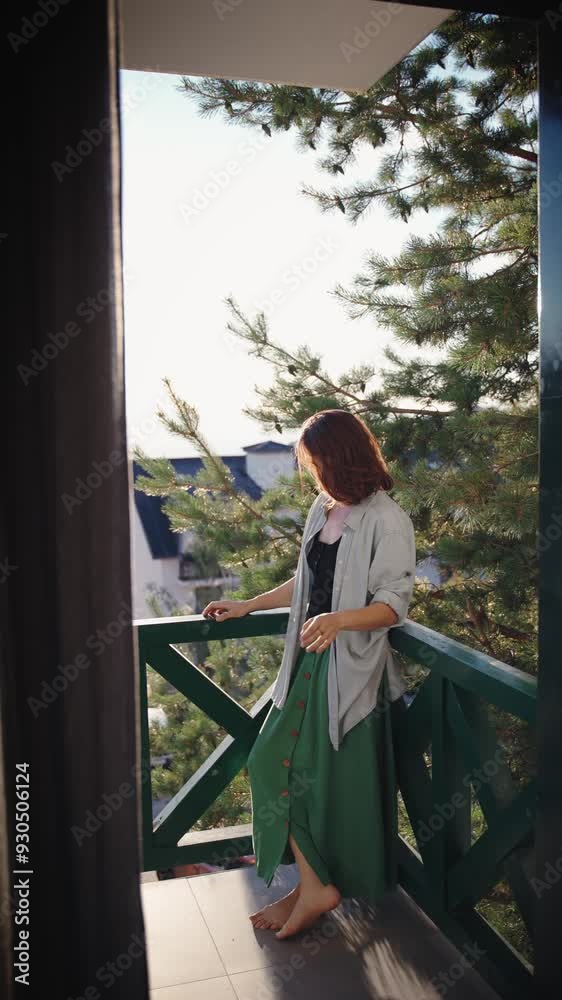 A vertical shot of a young woman enjoying the view of the mountains standing on the balcony during sunset. A vertical shot of a young woman enjoying the view of the mountains standing on the balcony during sunset.