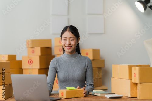 E-commerce Success: Asian businesswoman beaming with pride surrounded by packages and her laptop