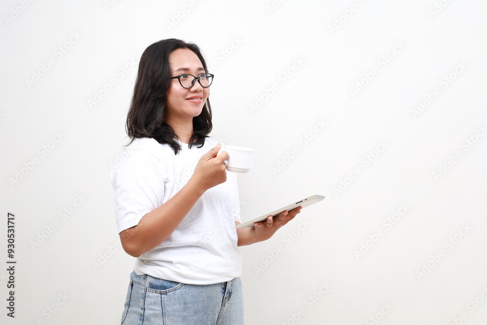 Attractive businesswoman drinking a coffee and using a digital tablet while standing over white background looking at empty space Attractive businesswoman drinking a coffee and using a digital tablet while standing over white background looking at empty space