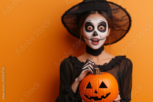 woman in Halloween disguise dancing isolated. The happy female in a skeleton costume and witch hat, with skull makeup, holding Jack's lantern pumpkin