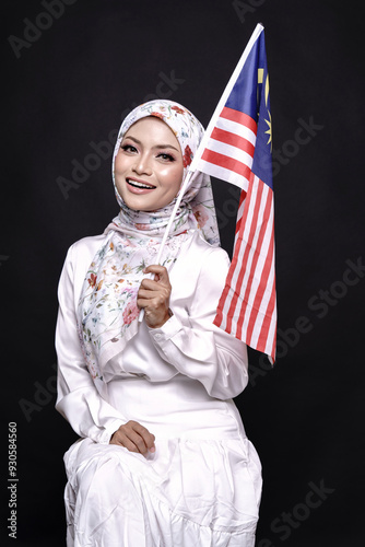 Beautiful Asian girl wearing white gress with hijab, happily holding Malaysian flag isolated over black background. Independence day, new year nationalism concept. photo