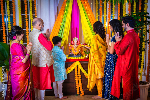 Indian Asian family performing Ganesh Puja at home in traditional attire, celebrating with devotion