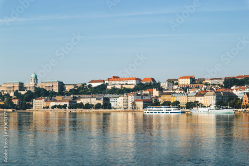 view of danube river in budapest with water reflection in summer with boats and beautiful colorful houses on clear sky