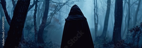 Silhouette of an individual in a dark cloak with a large hood navigating a mysterious forest, evoking feelings of fear, loneliness, and agoraphobia. photo