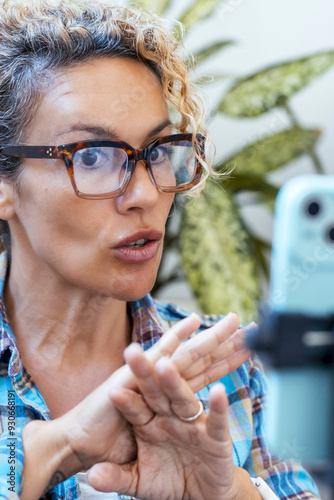 Female entrepreneur gesturing and speaking on a mobile phone while creating video content or conducting a videocall from home. A professional giving advice using voice and gestures in a digital worksp photo