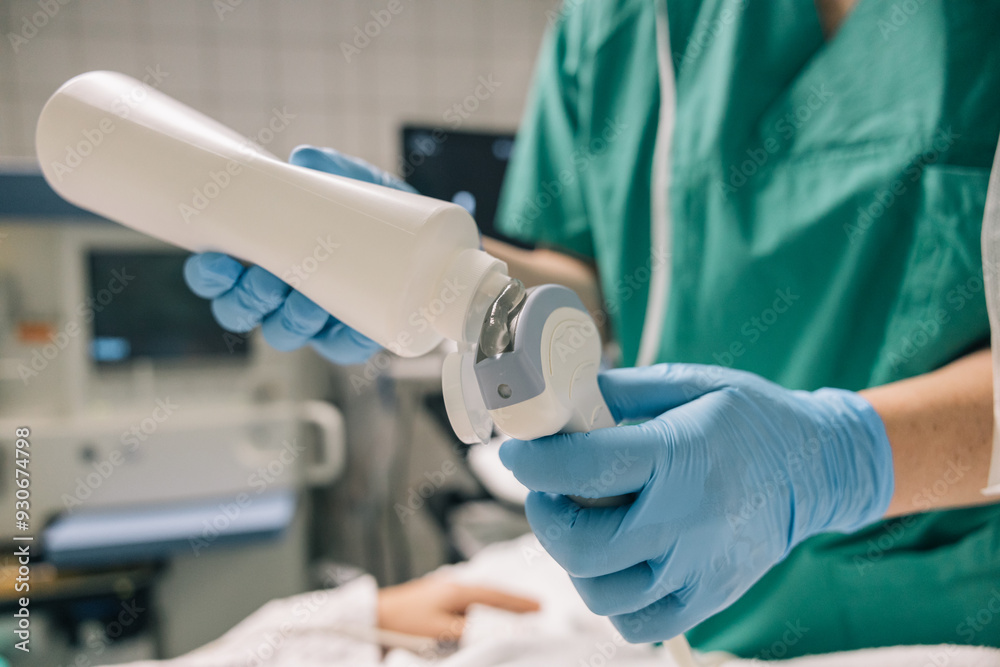 A medical worker in green scrubs and blue gloves prepares an ultrasound device with gel A medical worker in green scrubs and blue gloves prepares an ultrasound device with gel