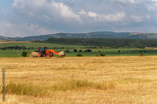 Tractor lifting hay bale on barrow.