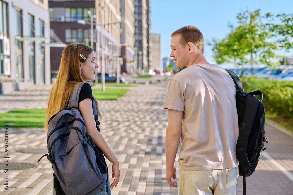 Fototapeta premium Guy and girl, college students walking together along street of city, back view