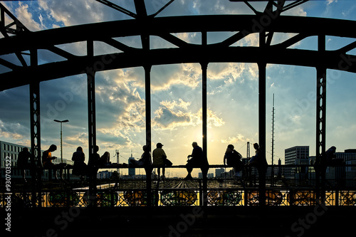 Silhouettes of young people sitting on the steel bridge in the sunset