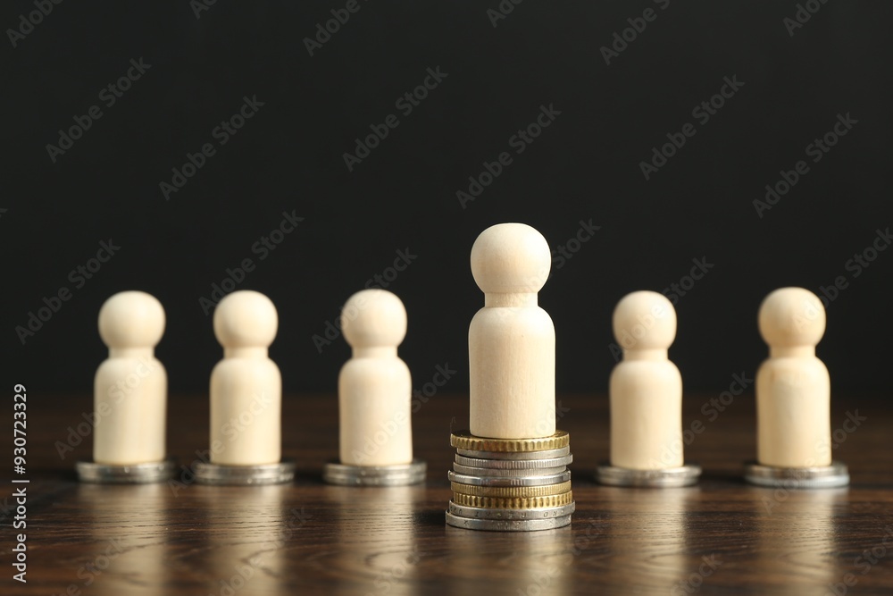Financial inequality. One wooden figure with bigger stack of coins than others on table Financial inequality. One wooden figure with bigger stack of coins than others on table