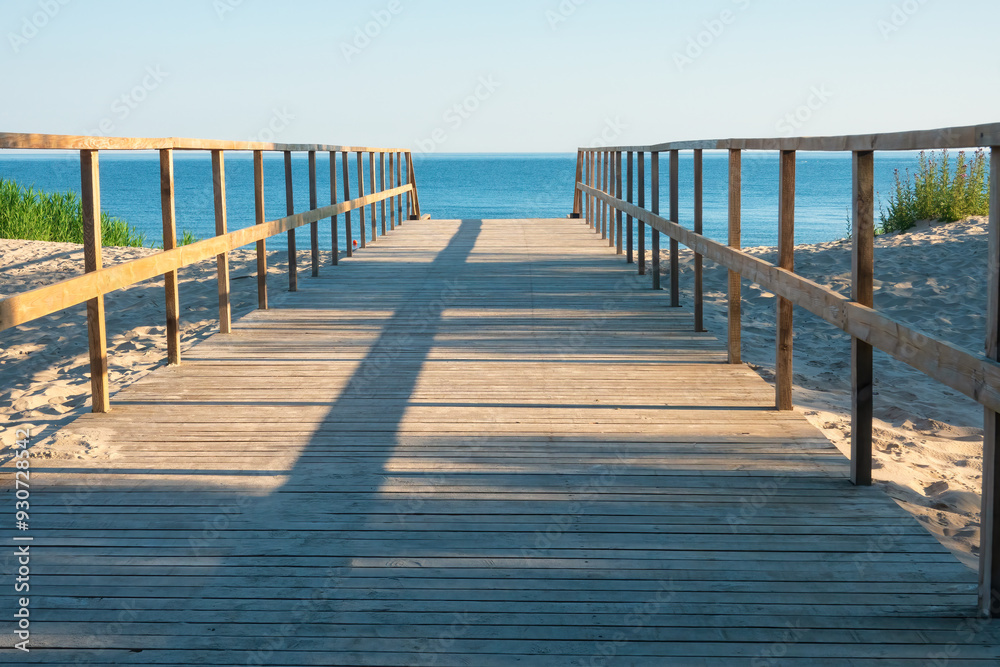 Perspective view of simple wooden path across sand dune. Sea and sky are visible. Background. Landscape.