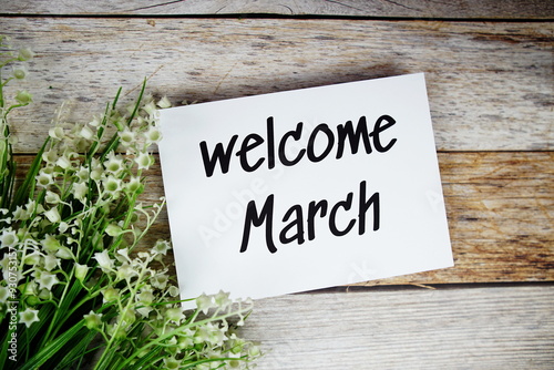 Welcome March text on paper card with flowers frame top view on wooden background