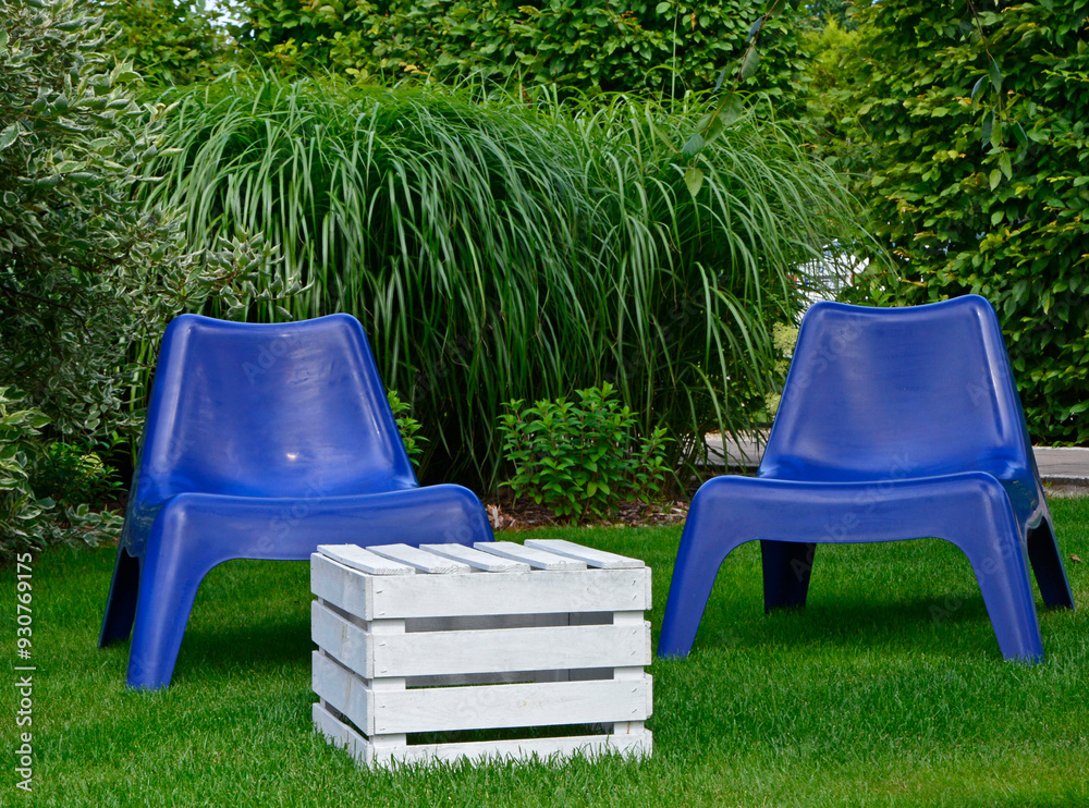 biały stolik ze skrzynki i niebieskie fotele ogrodowe na trawie, blue plastic garden chair on grass, garden table made of box, blue chairs and white wooden box in garden, fotel ogrodowy