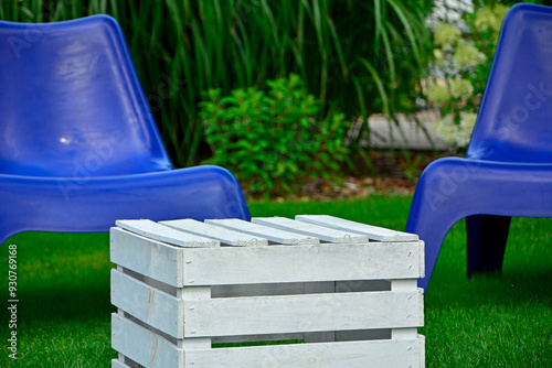 Obraz na płótnie biały stolik ze skrzynki i niebieskie fotele ogrodowe na trawie, blue plastic garden chair on grass, garden table made of box, blue chairs and white wooden box in garden, fotel ogrodowy