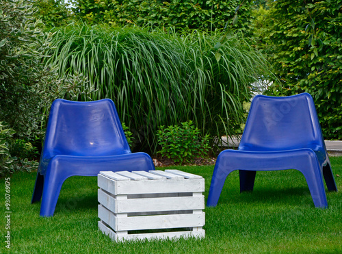 Obraz na płótnie biały stolik ze skrzynki i niebieskie fotele ogrodowe na trawie, blue plastic garden chair on grass, garden table made of box, blue chairs and white wooden box in garden, fotel ogrodowy