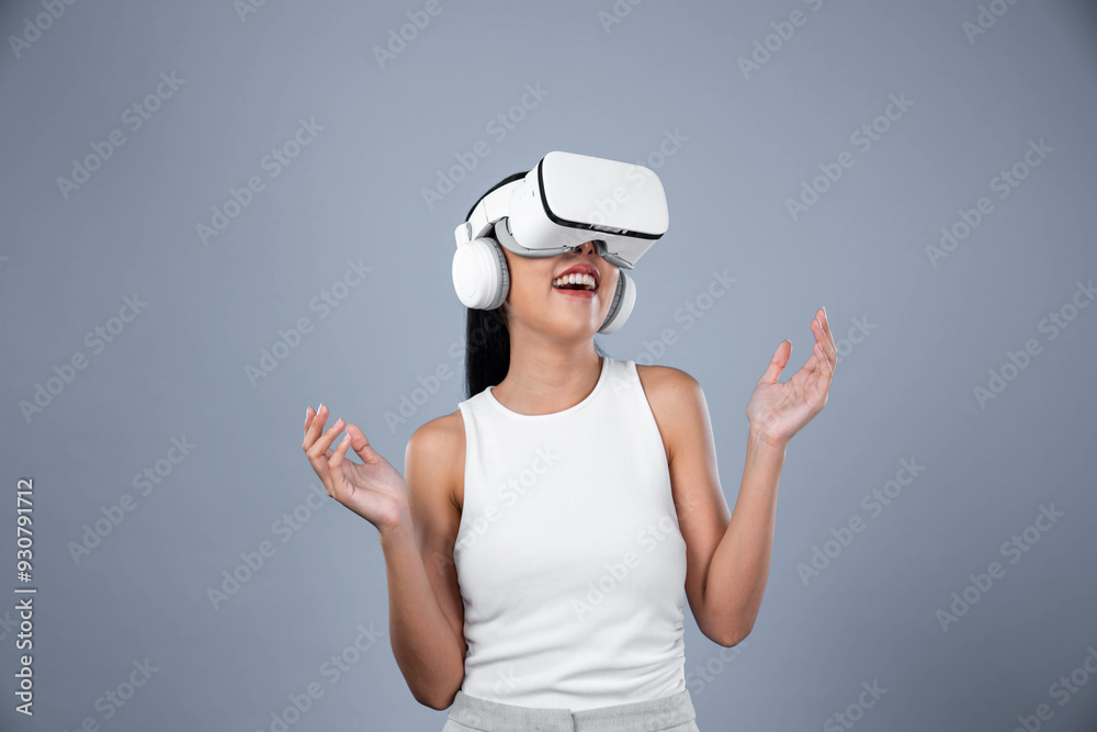 Smart female standing with gray background wearing VR headset connecting metaverse, futuristic cyberspace community technology. Elegant woman excited seeing generated virtual scenery. Hallucination. Smart female standing with gray background wearing VR headset connecting metaverse, futuristic cyberspace community technology. Elegant woman excited seeing generated virtual scenery. Hallucination.
