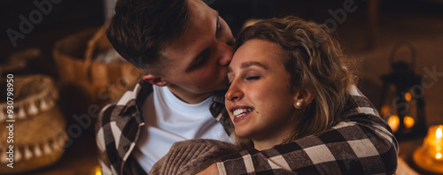 Beautiful young loving couple relaxing near fireplace in bed at home. Happy spouses enjoying lazy romantic winter cozy morning in bedroom. Candles, garlands, countryside interior. Romantic date banner