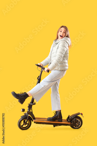 Young woman riding electric scooter on yellow background