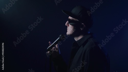 Rap artist singing into a microphone for a music video on a dark background