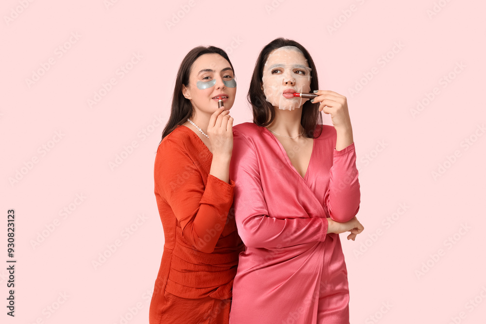 Beautiful young women with facial mask and under-eye patches applying lipsticks on pink background Beautiful young women with facial mask and under-eye patches applying lipsticks on pink background