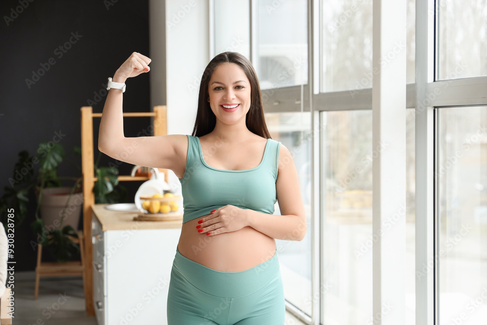 Sporty pregnant woman showing muscles near window at home Sporty pregnant woman showing muscles near window at home
