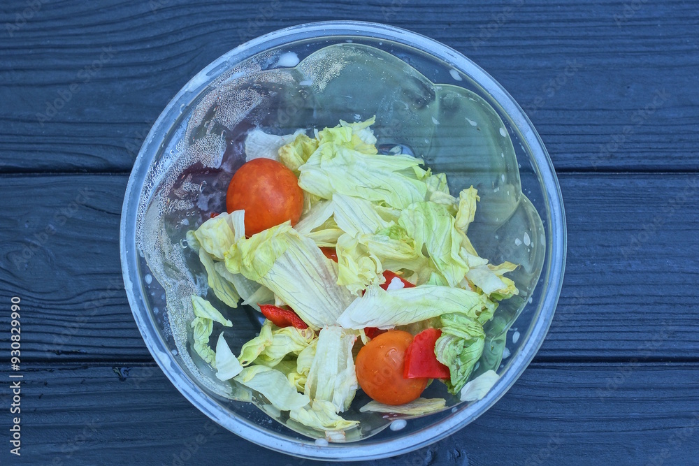 food from fresh green salad and red tomatoes in a plastic plate stands on a black wooden table food from fresh green salad and red tomatoes in a plastic plate stands on a black wooden table