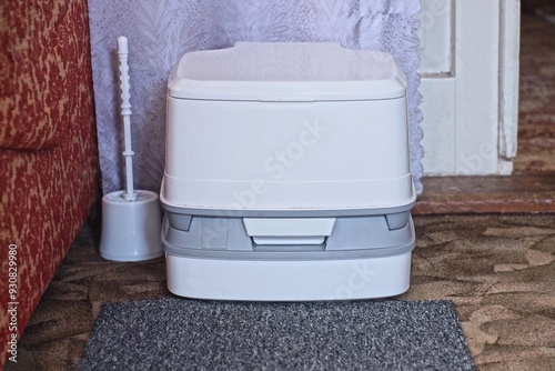 one white closed compact plastic bio-toilet stands on a gray carpet on the floor in the room photo