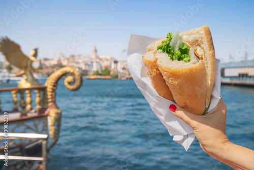 Canvas Print Tourist hand with balik ekmek fish sandwich with stunning views of the Bosphorus and Istanbul city skyline