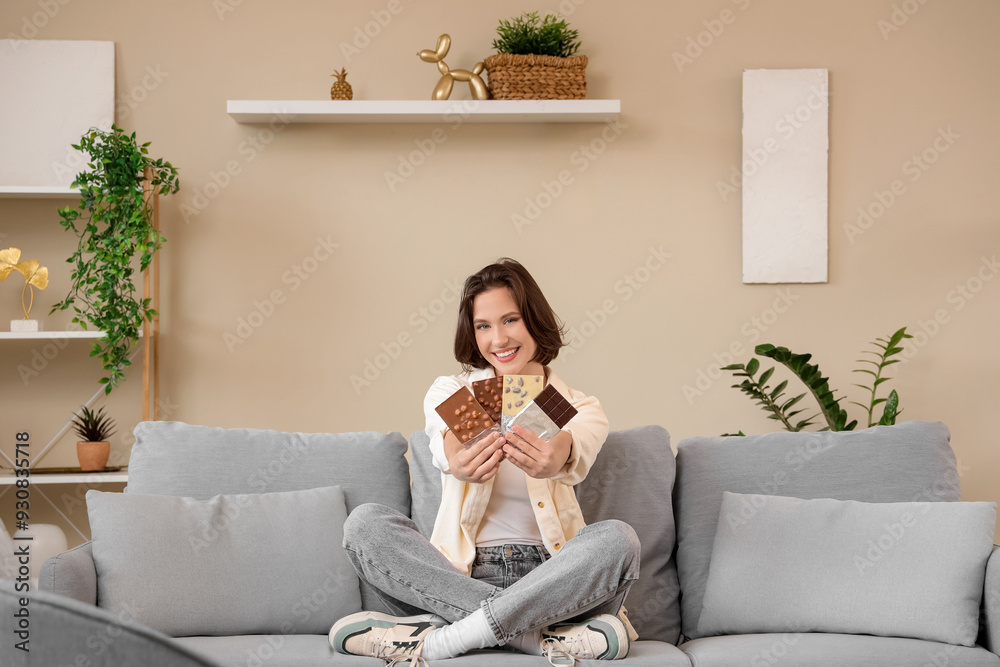 Beautiful young happy woman with different tasty chocolate bars sitting on sofa at home Beautiful young happy woman with different tasty chocolate bars sitting on sofa at home