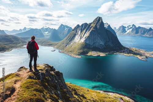 Hiker on a mountain peak overlooking Lofoten Islands in Norway, with turquoise waters and rugged cliffs, embodying adventure and exploration.