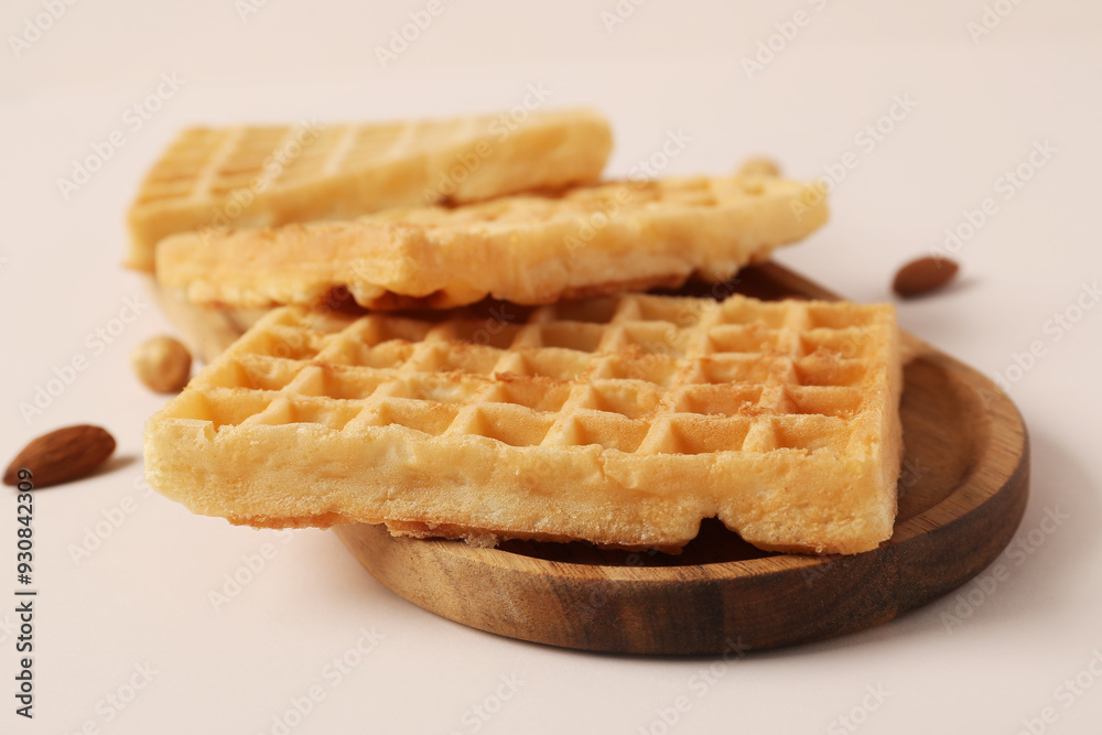 Wooden board with tasty Belgian waffles and nuts on beige background Wooden board with tasty Belgian waffles and nuts on beige background